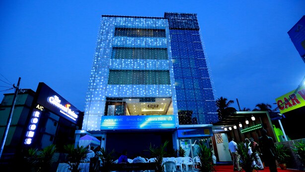 A modern building with a glass facade, a red carpet entrance, and outdoor seating area with tables and chairs. - The Crescent Suites (Kanayannur)