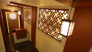 A hallway with a reception desk, a decorative wooden partition, and a hanging lantern. - The Crescent Suites (Kanayannur)