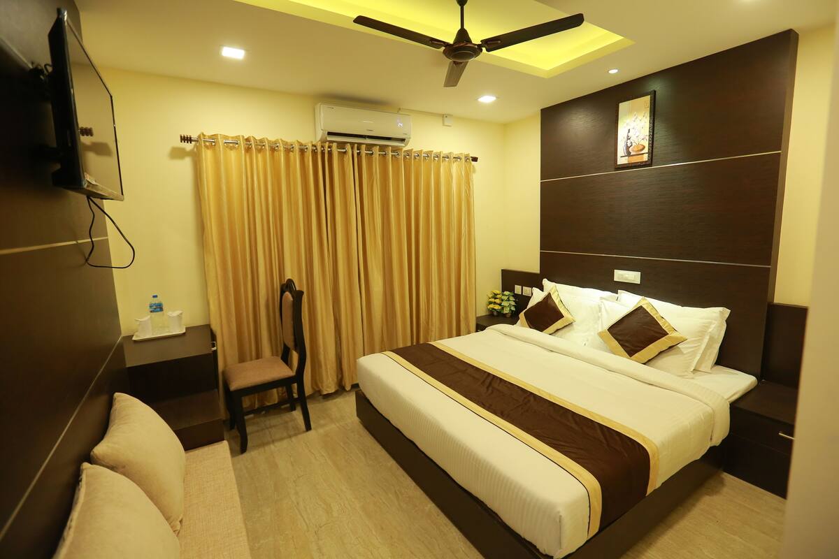 A hotel room with a bed, a chair, a desk, an air conditioner, and a ceiling fan.