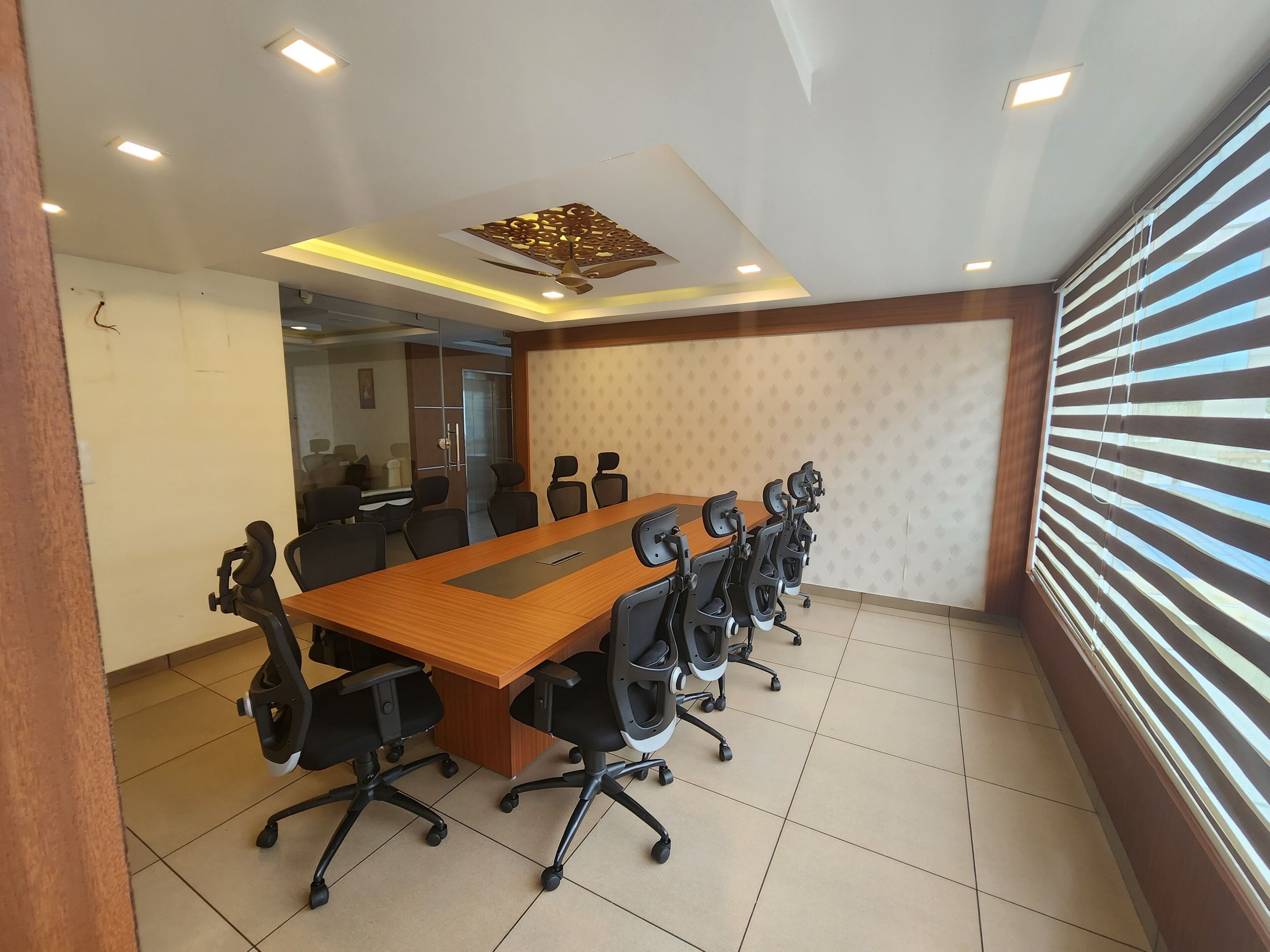 A conference room with a long wooden table, black office chairs, and a ceiling with recessed lighting and a decorative panel.
