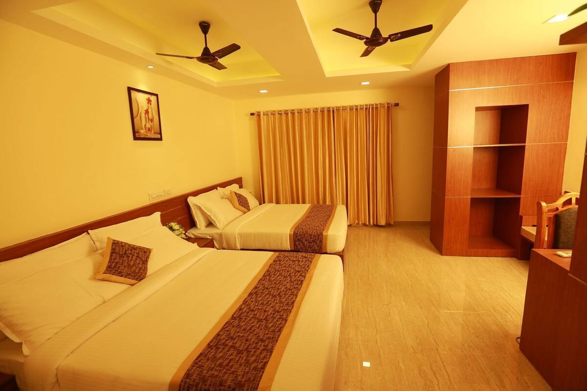 A hotel room with two beds, a ceiling fan, a large window with curtains, and a wooden wardrobe.
