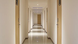 A hotel hallway with a polished floor, wooden doors, and a neutral color scheme. - ROOM Hotel & Suites (Puebla)