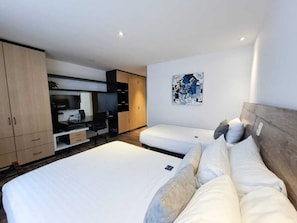 A hotel room with a bed, a desk, a TV, and a painting on the wall. - ROOM Hotel & Suites (Puebla)