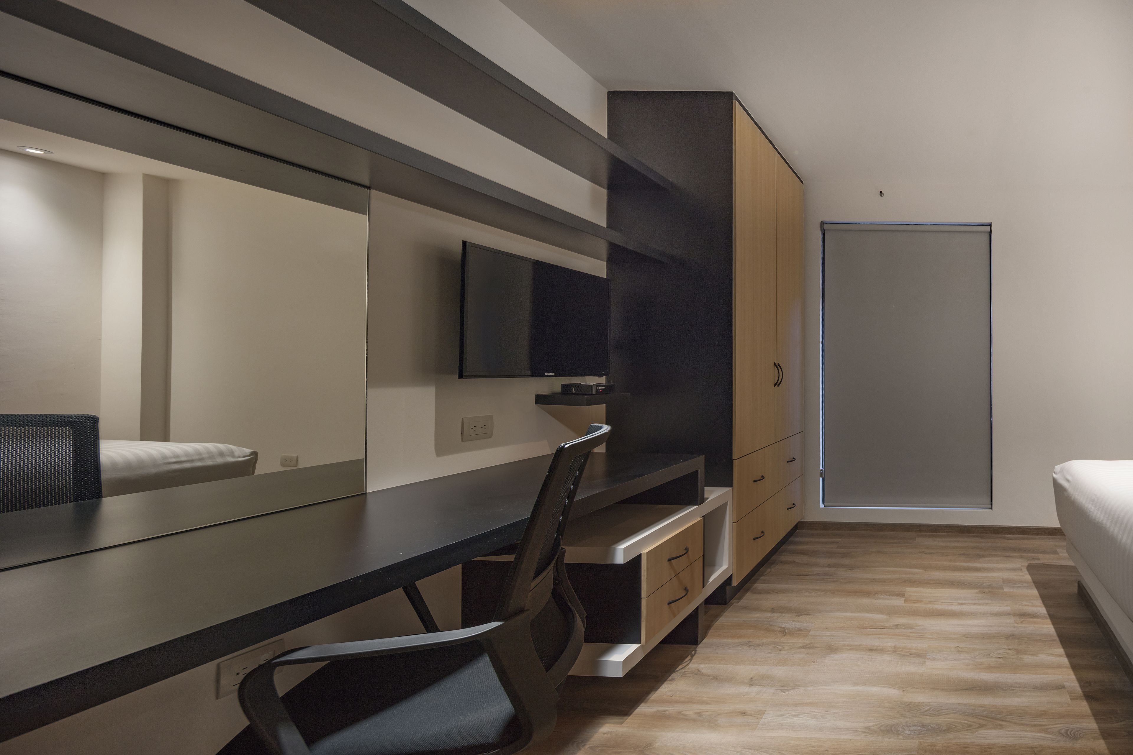 A modern bedroom with a bed, a desk, a chair, a wardrobe, and a television.