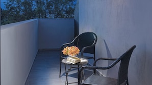 A balcony with two wicker chairs, a small table with a book and a vase of flowers, and a view of trees and sky. - ROOM Hotel & Suites (Puebla)