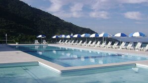 Une piscine entourée de chaises longues et de parasols, le tout niché au cœur d’un paysage montagneux.