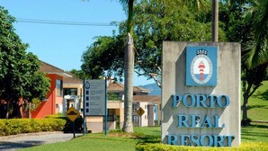 Une enseigne pour le Porto Real Resort, avec son logo, entourée de verdure et de bâtiments.