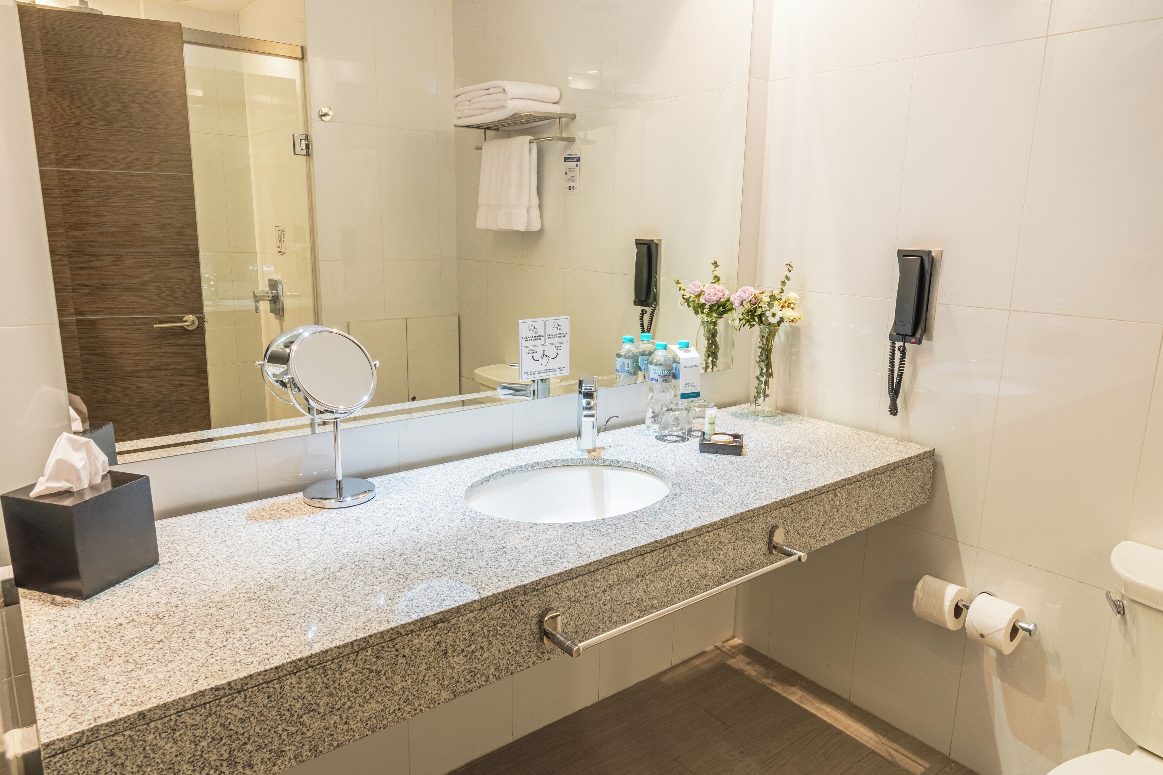 Un baño moderno con encimera de granito, un lavabo, un espejo, un perchero para toallas, un inodoro y un teléfono.