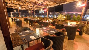 An outdoor restaurant with wicker furniture, tables with menus, and a city view at night. - Sonesta Hotel Arequipa (Arequipa)