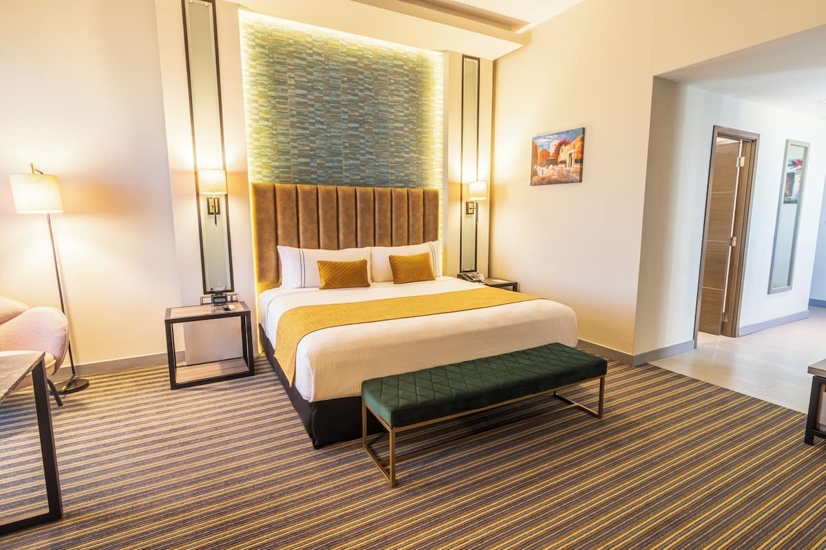 A hotel room with a large bed, bedside tables, a bench, and a carpeted floor.