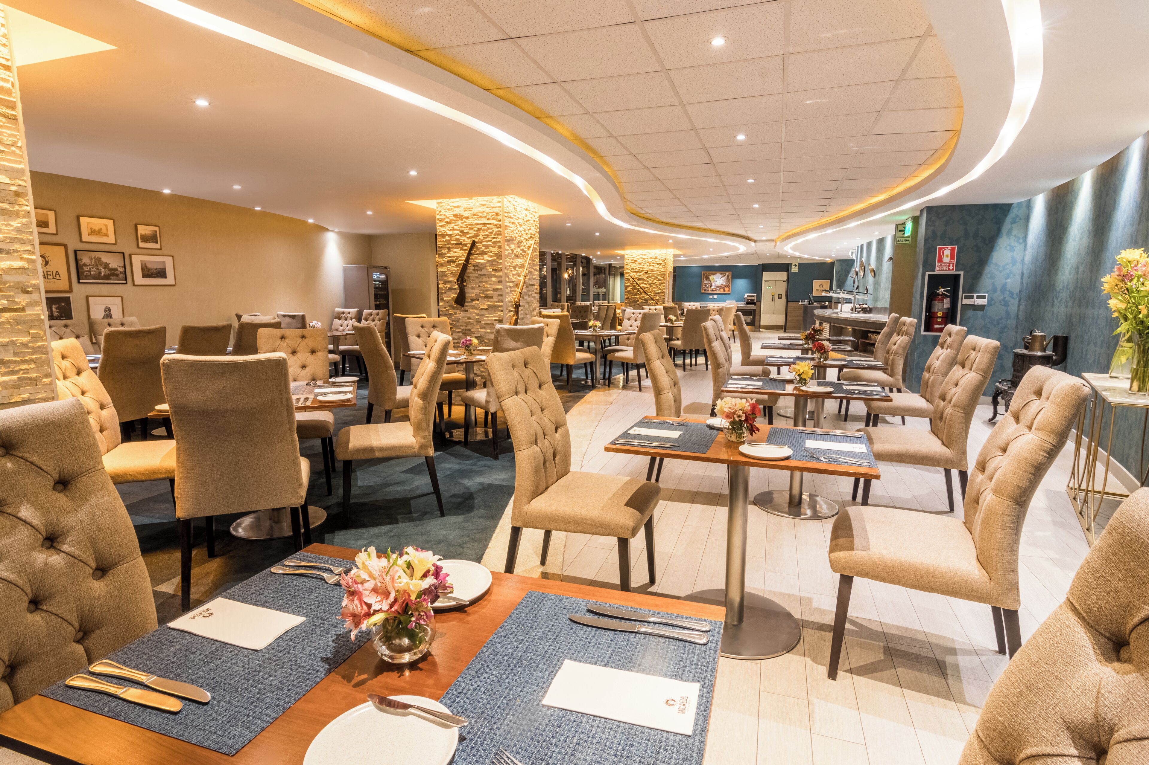 Un restaurante espacioso con sillas de respaldo alto, mesas redondas y un diseño de interiores moderno.