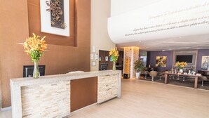 A reception area with a stone counter, two vases with flowers, framed artwork on the wall, and a large text display. - Sonesta Hotel Arequipa (Arequipa)