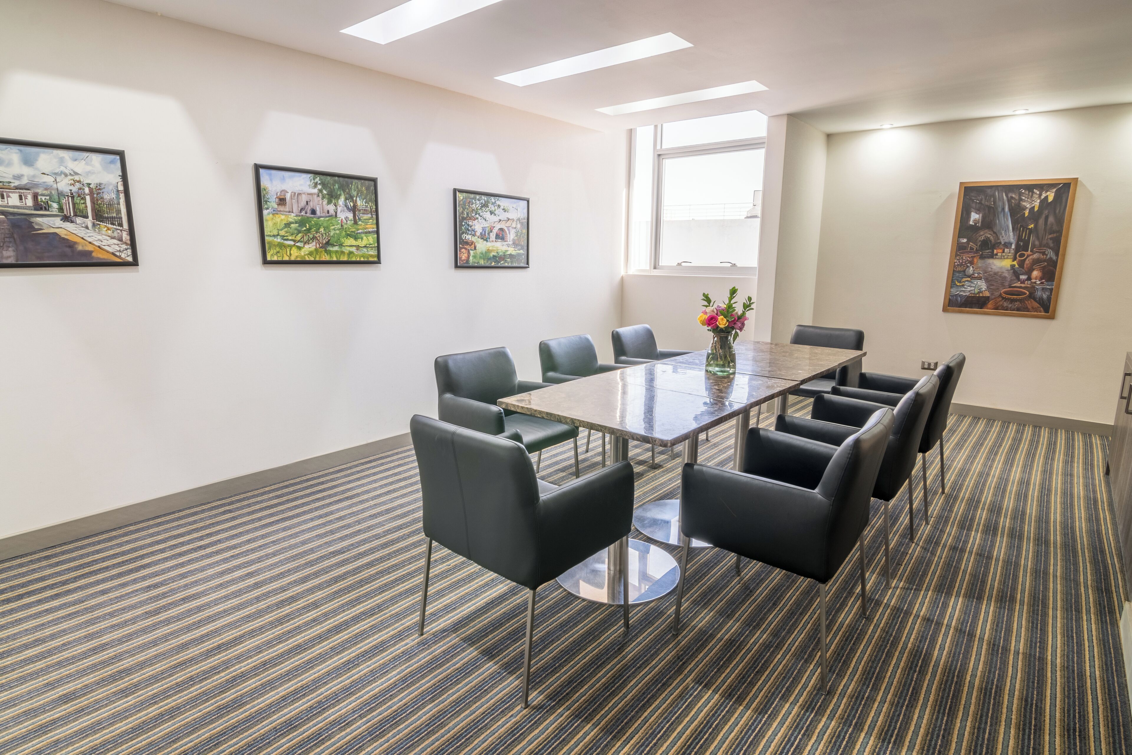 A conference room with a glass table, black chairs, and artwork on the walls.