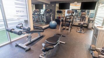 Un gimnasio con máquinas de cardio, equipo de levantamiento de pesas y un espejo grande.