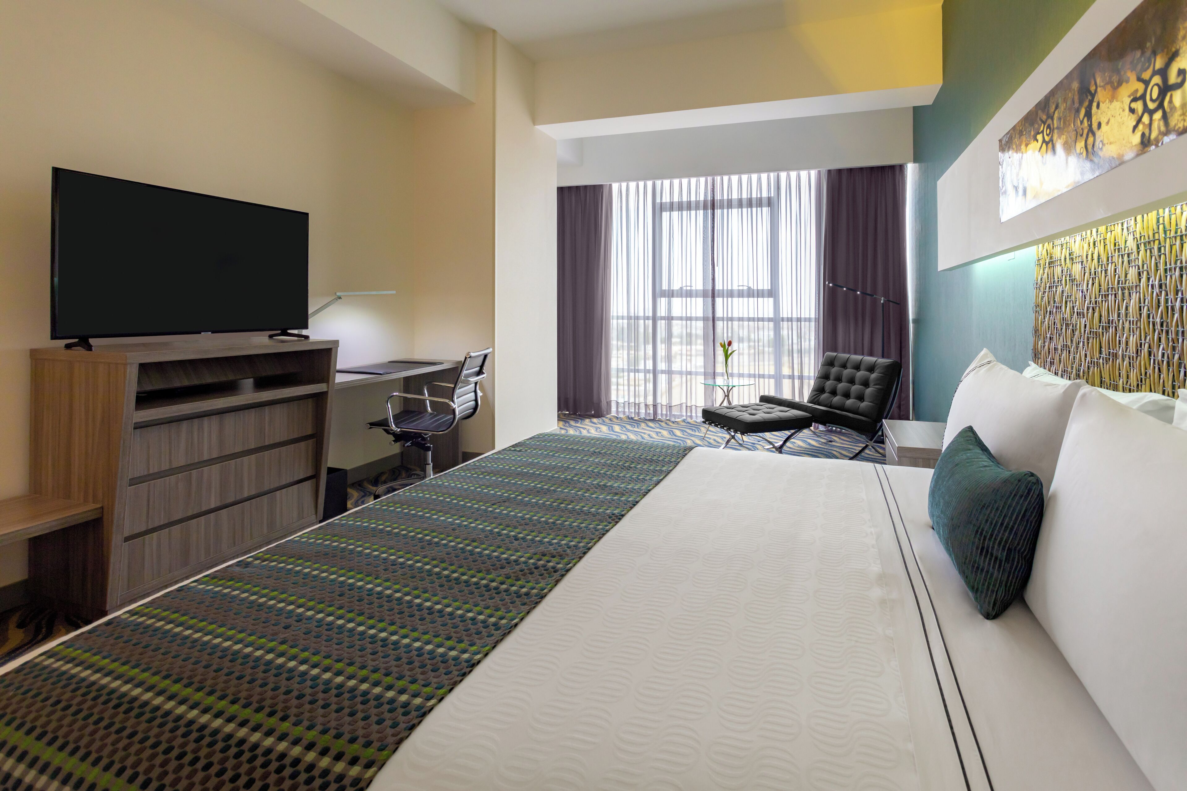 A hotel room with a large bed, a desk with a chair, a television, and a window with curtains.