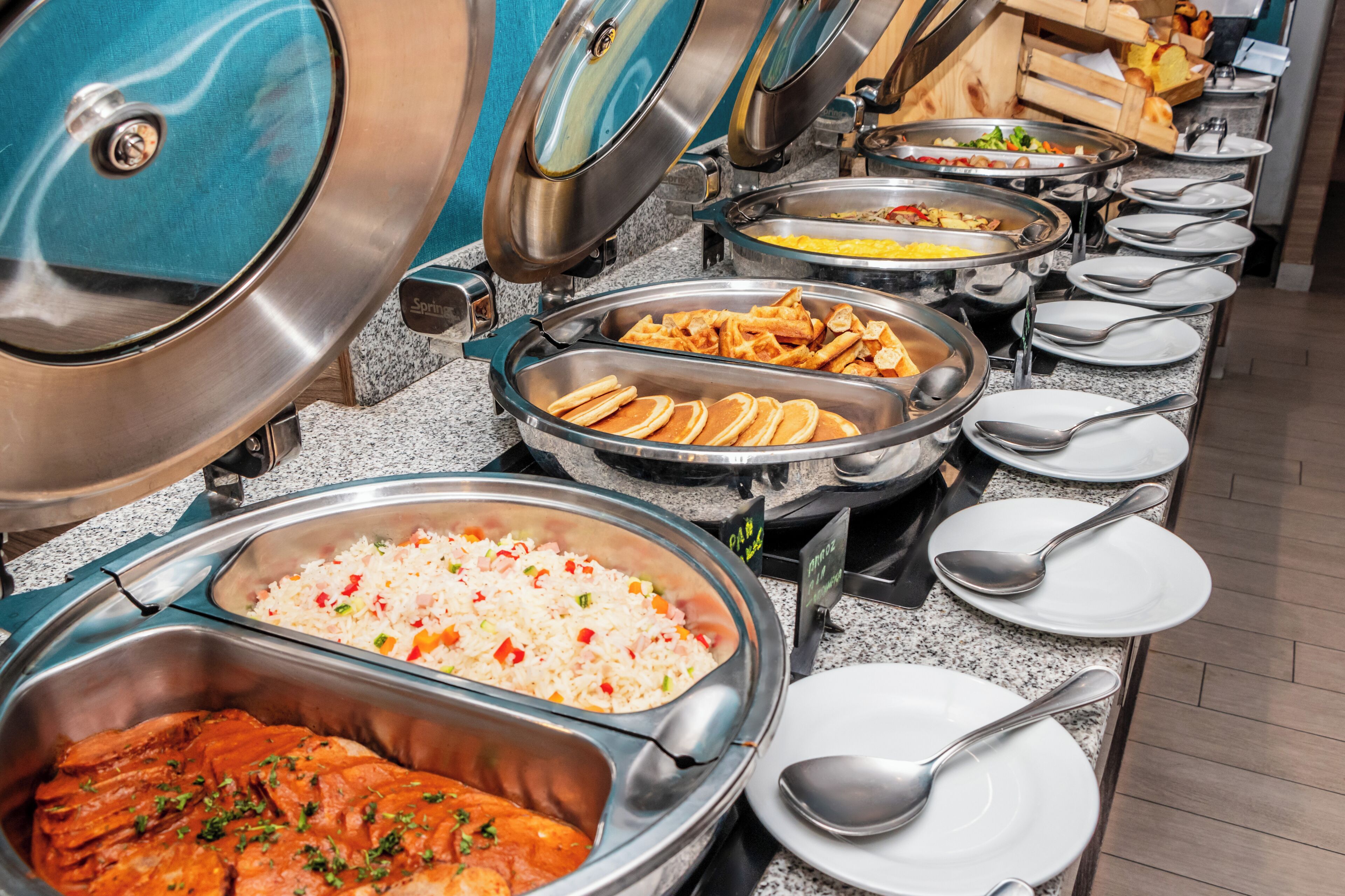 Un bufé con diversas opciones de comida, incluyendo arroz, pollo, gofres y vegetales.