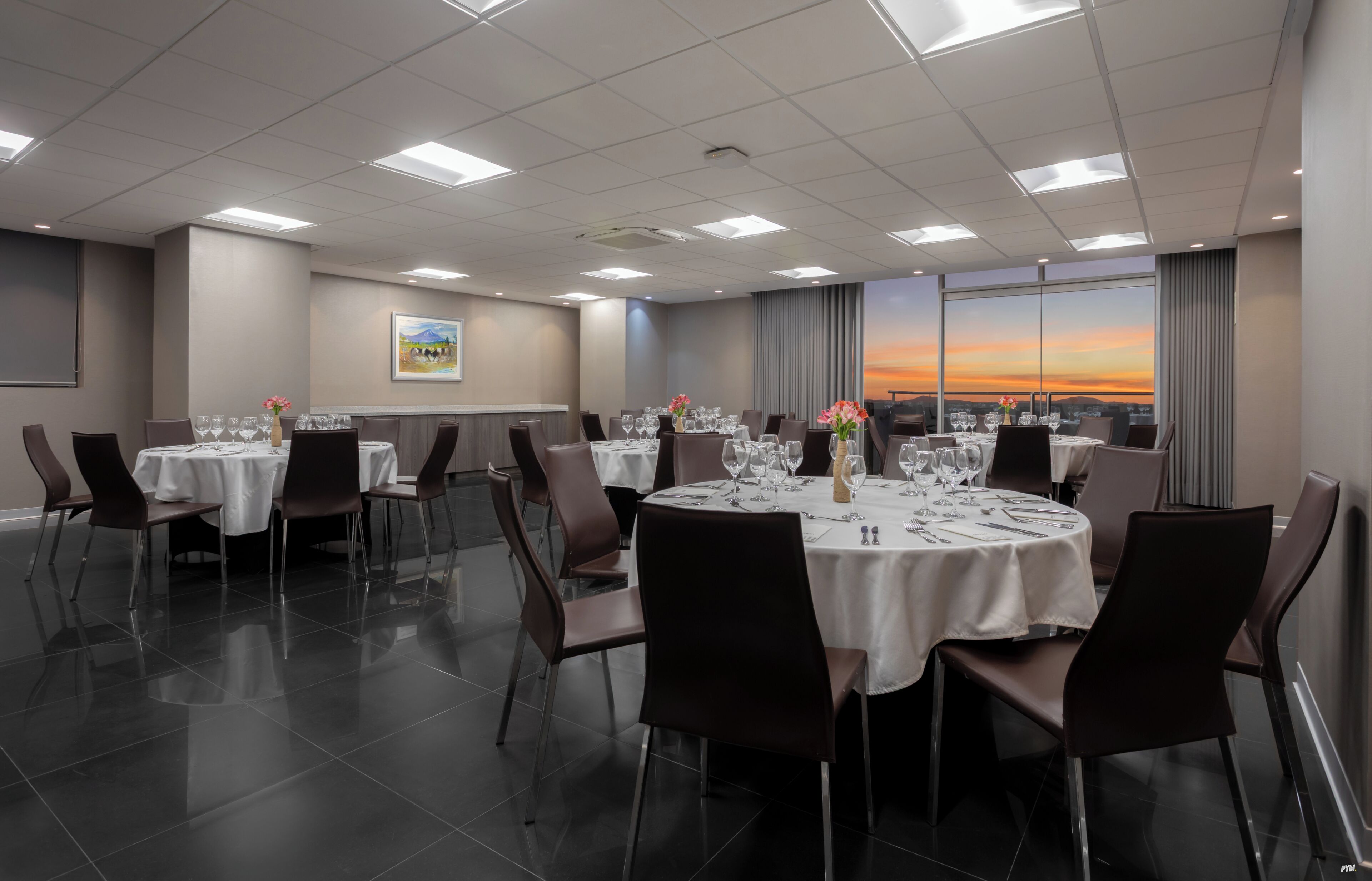 A conference room with round tables, chairs, and a painting on the wall.