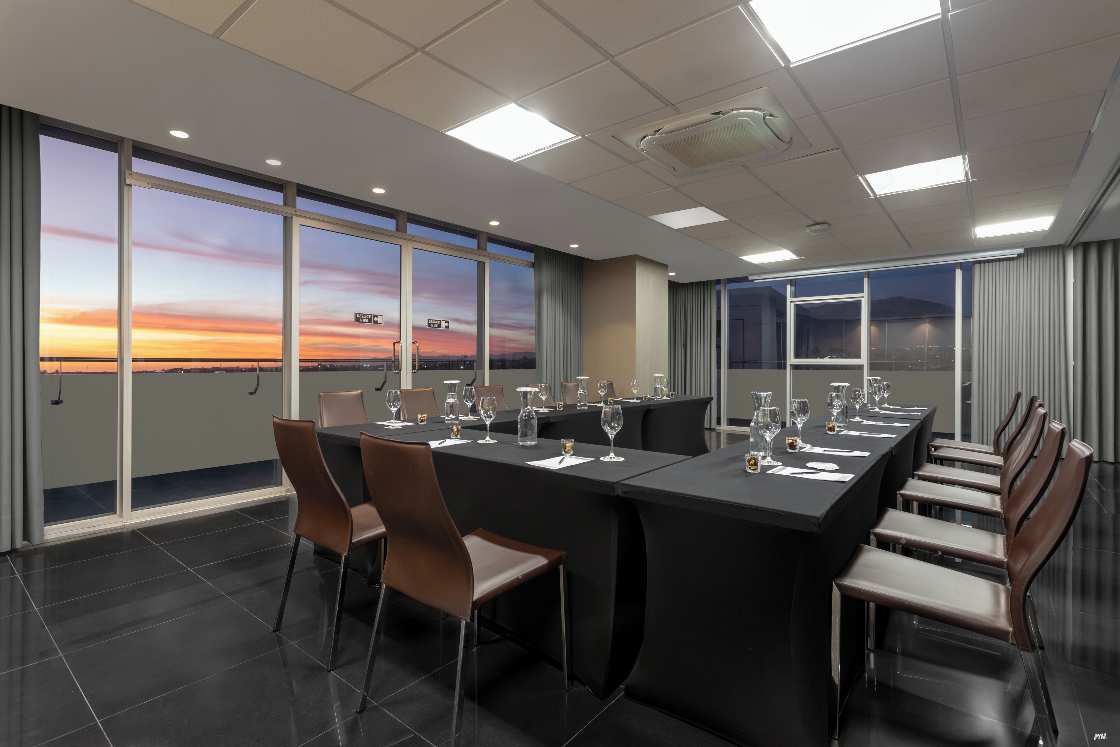 Ein Konferenzraum mit großem Tisch, Stühlen und Blick auf einen Sonnenuntergang durch die Fenster.