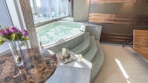 A spa area with a hot tub, a marble table with a vase of flowers, and a view of the city through large windows. - Sonesta Hotel Arequipa (Arequipa)