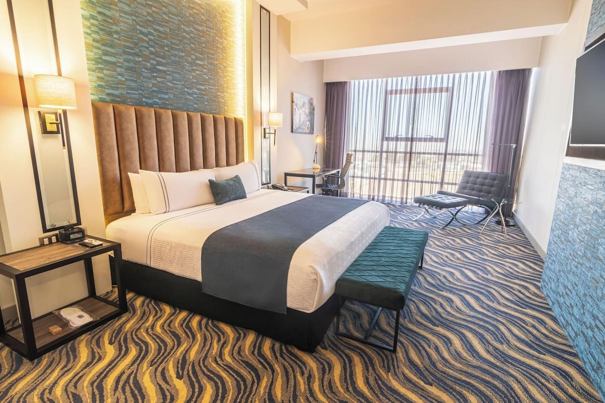 A hotel room with a large bed, a desk, a chair, and a view of the outdoors.