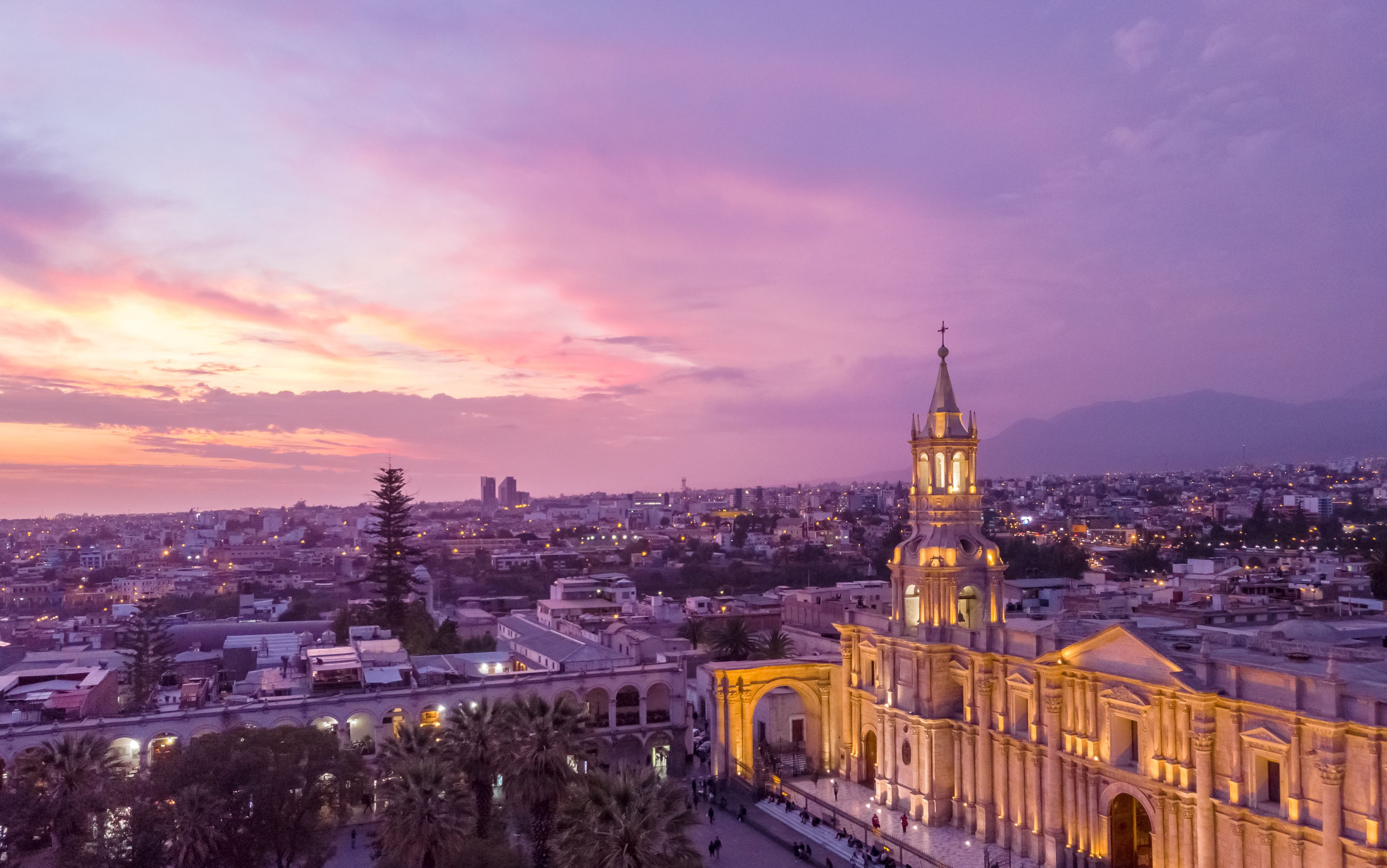 A cityscape at dusk with a prominent illuminated church featuring a tall bell tower and arches.