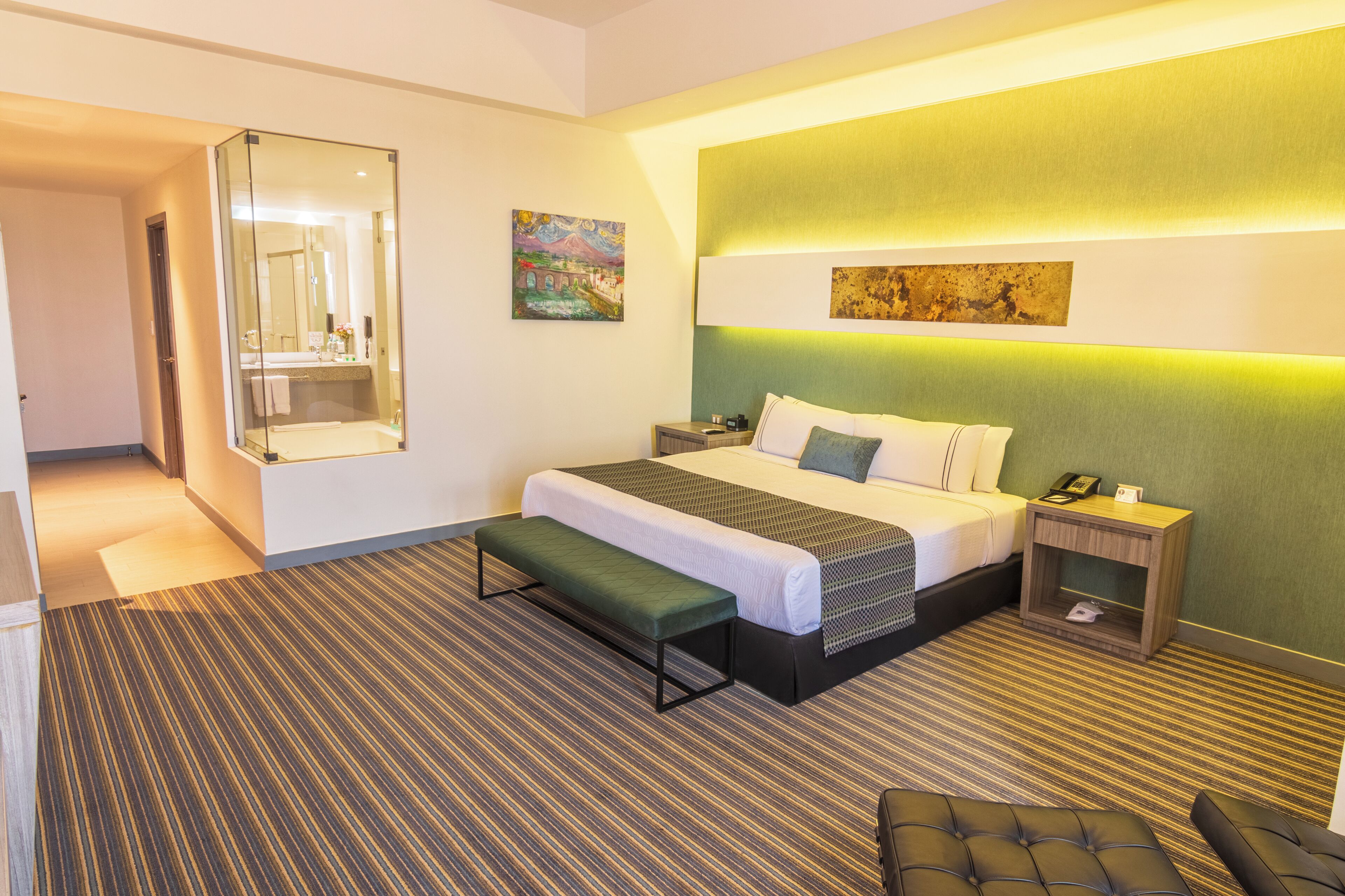 Una habitación de hotel con cama, mesita de noche, banco y un espejo grande.