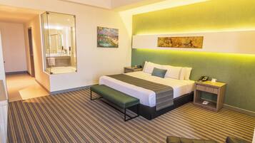 Una habitación de hotel con cama, mesita de noche, banco y un espejo grande.
