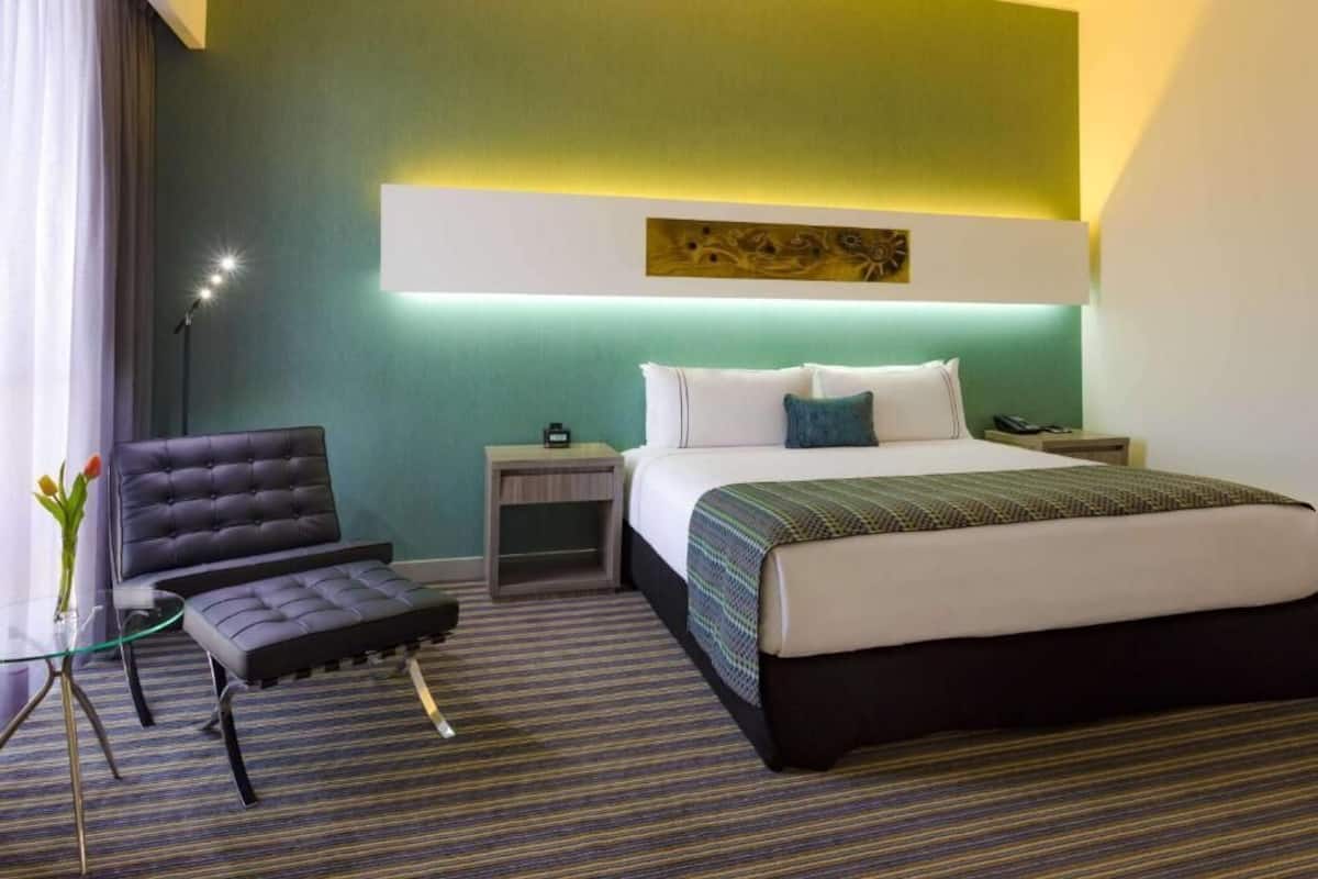 A hotel room with a bed, a chair, a nightstand, and a lamp.
