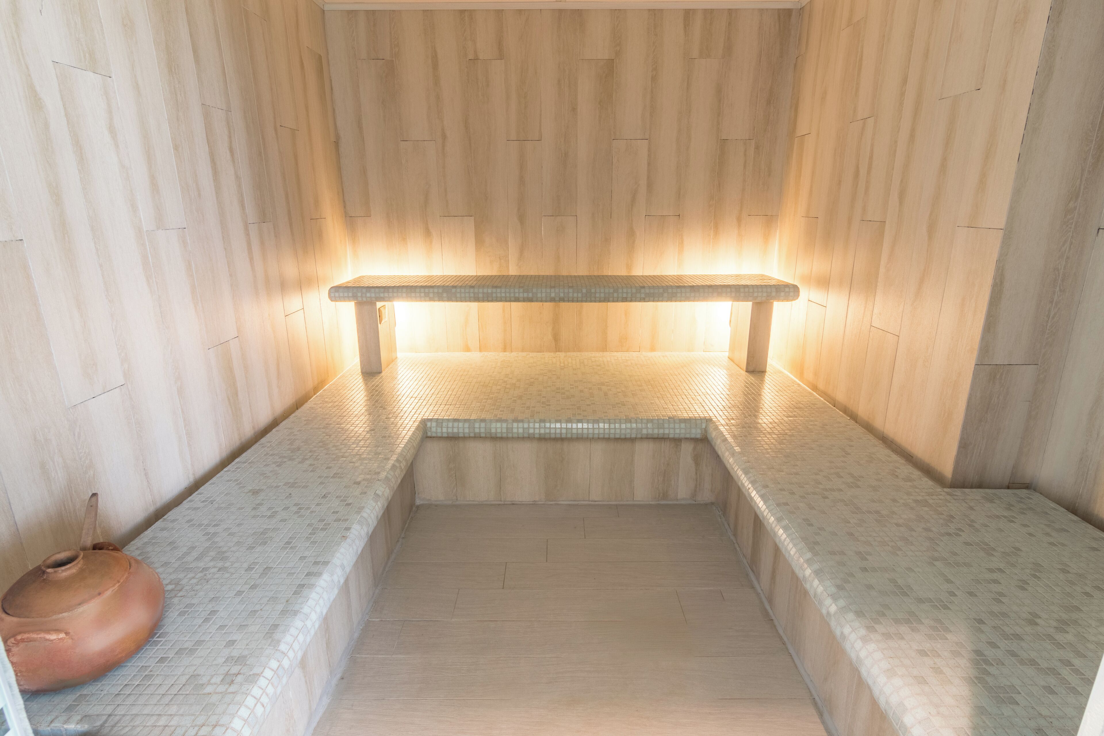A sauna with a bench, tiled walls, and a wooden floor.