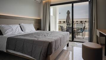 Quarto de hotel moderno com uma cama grande, uma mesinha e varanda com área de estar.