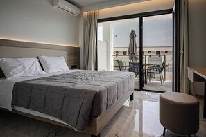 Una habitación de hotel moderna con una cama grande, una mesita pequeña y un balcón con mobiliario de exterior.