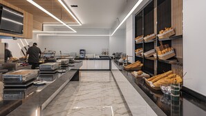 A modern kitchen with marble countertops, a central island, and shelves stocked with bread. - Caretta Paradise Resort & Waterpark (Zakynthos)