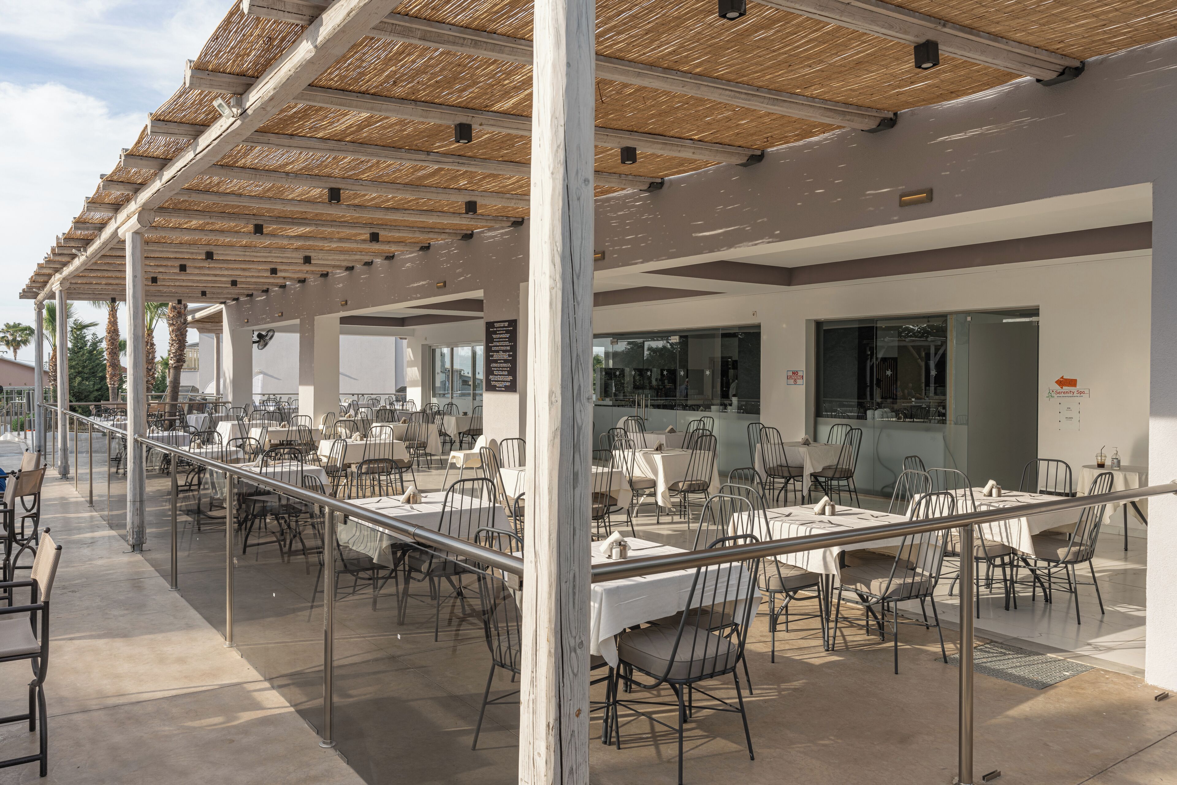 An outdoor dining area with tables and chairs, a covered seating area with a thatched roof, and a view of the street.