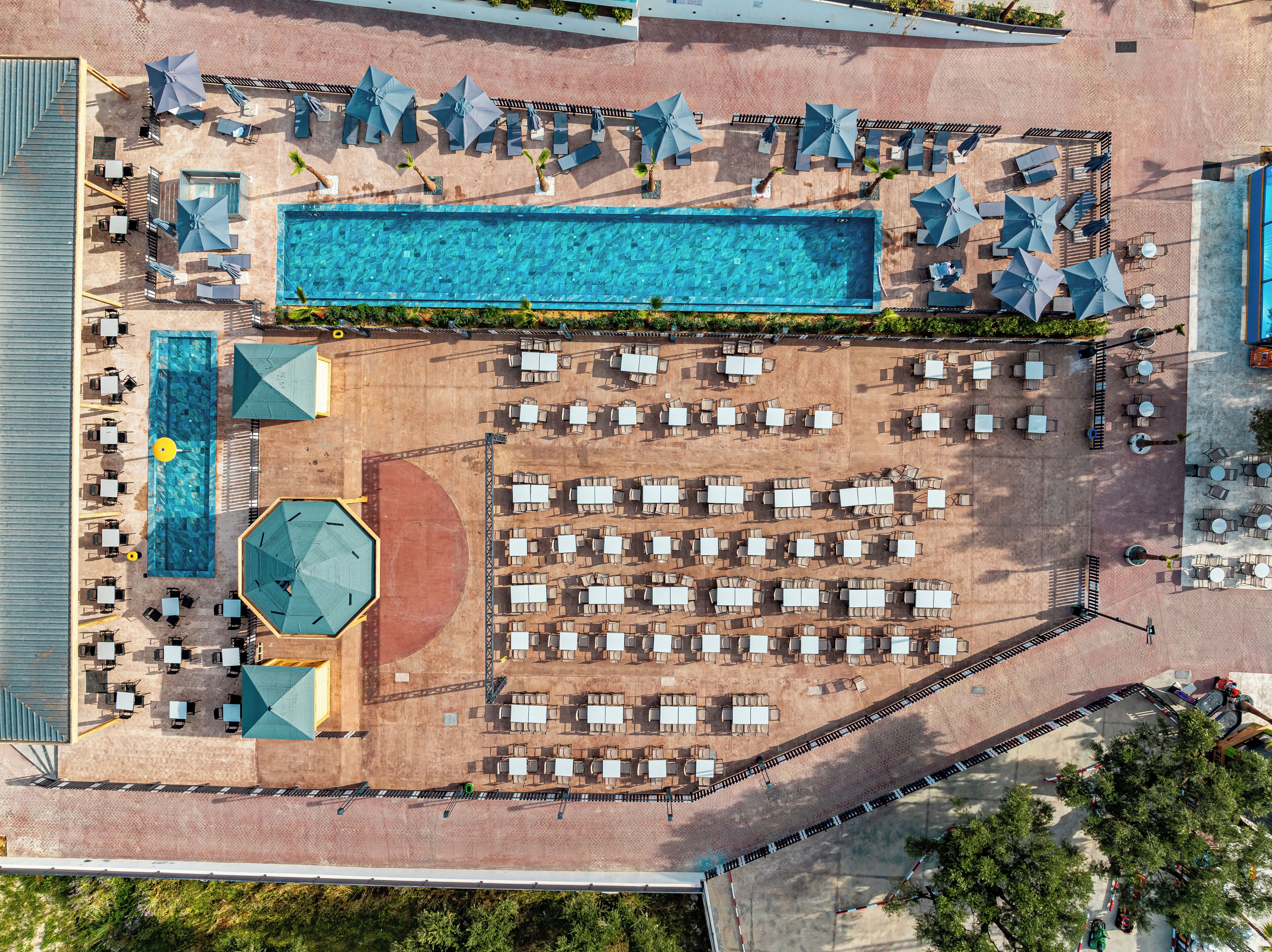 An aerial view of a resort with a swimming pool, multiple lounge areas, and outdoor seating.