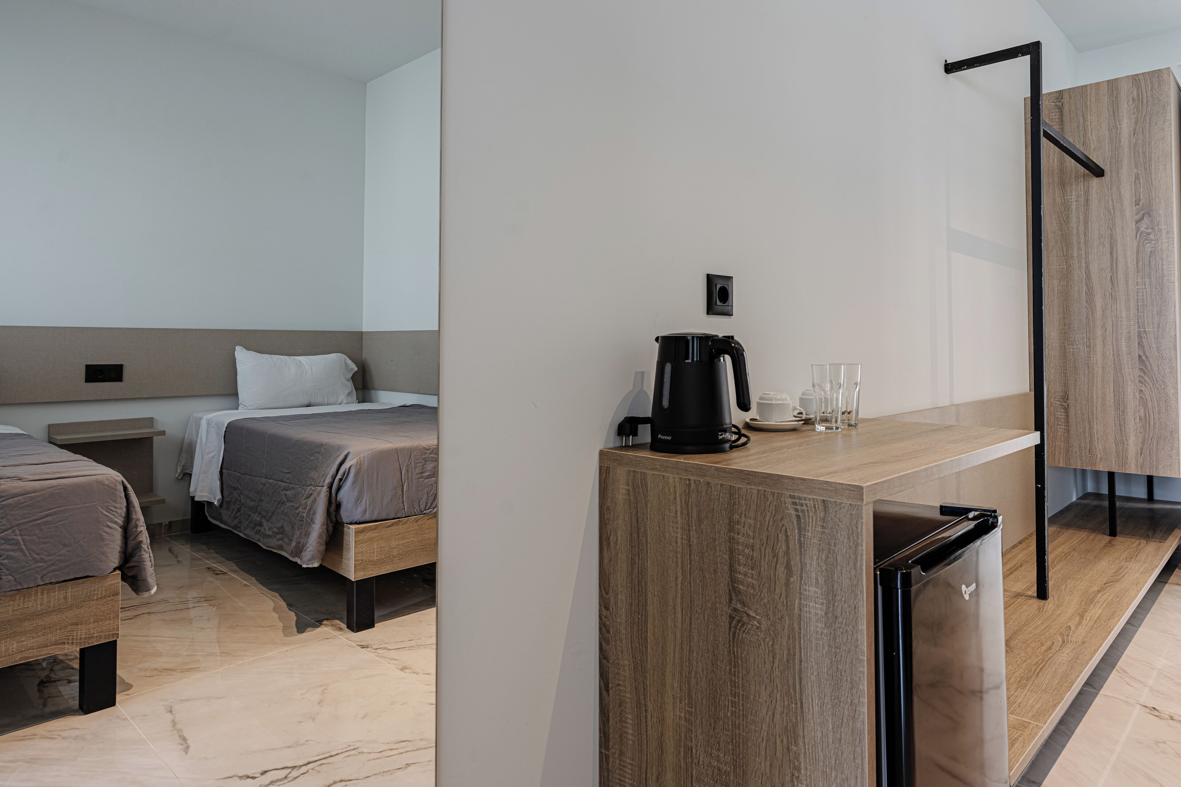 A modern hotel room with two beds, a wooden desk, a coffee maker, and a refrigerator.