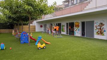 Zona de juegos infantiles con tobogán, pared de escalar y varios juguetes sobre césped artificial.