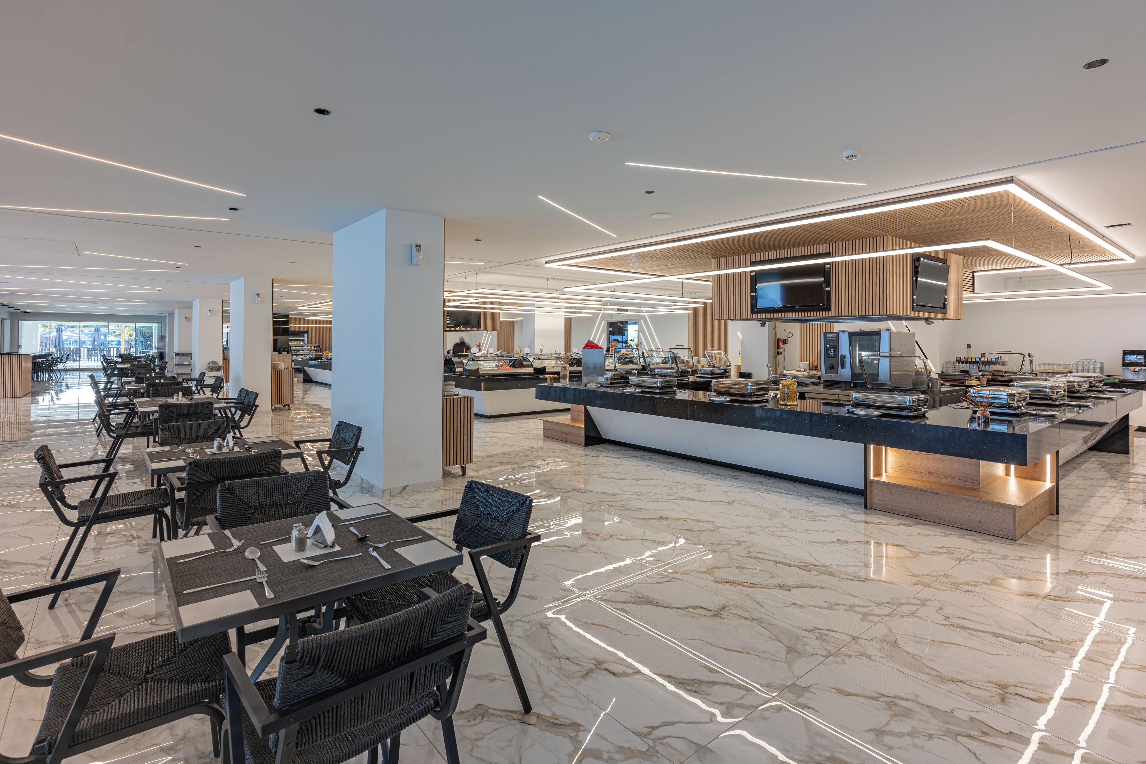 Un hall d’hôtel moderne avec un espace de restauration central, un comptoir d’accueil et une cuisine en arrière-plan.