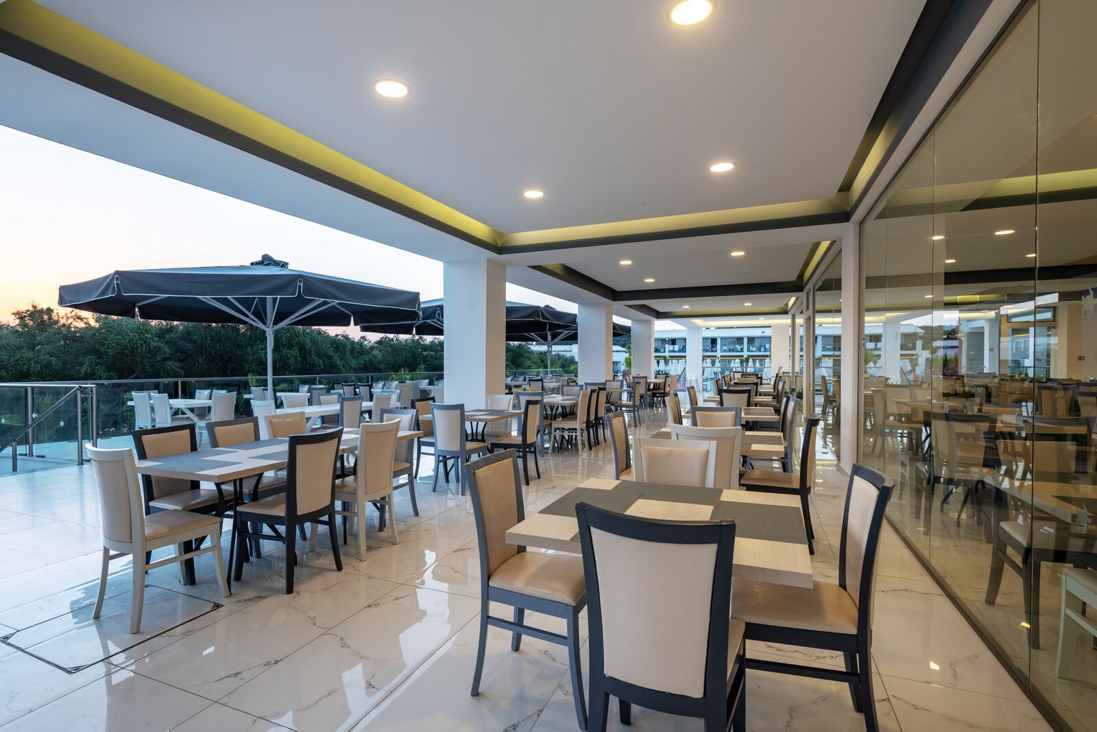 An outdoor dining area with tables and chairs, a glass wall, and a view of the surrounding landscape.