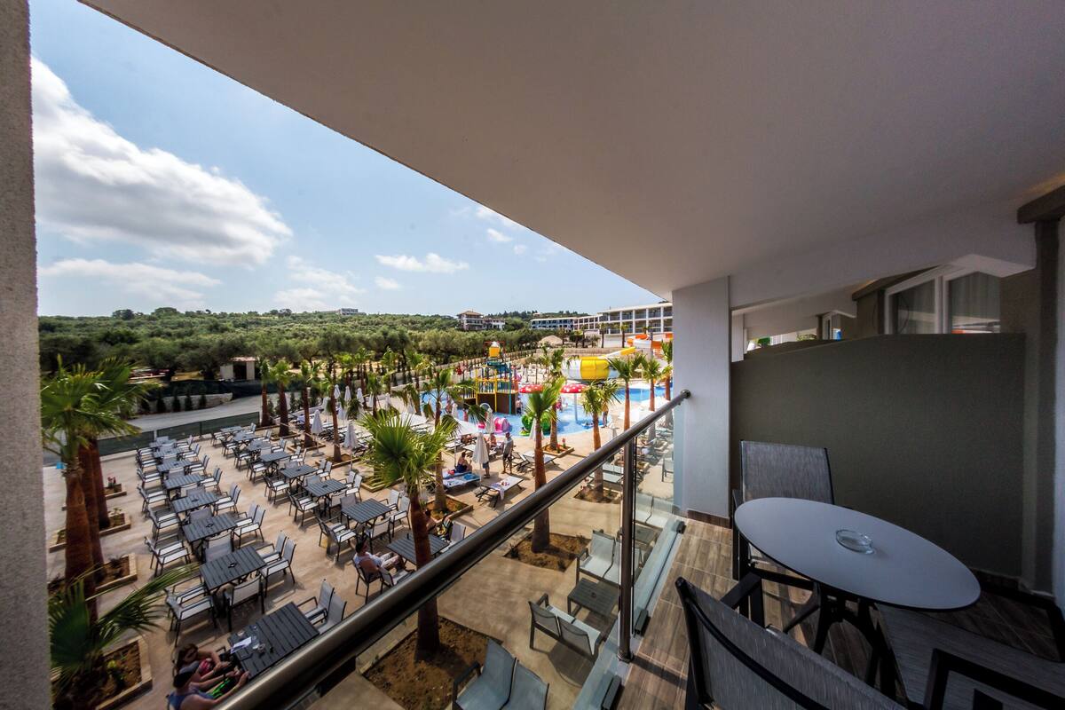 A balcony with a view of a pool area, outdoor seating, and palm trees.