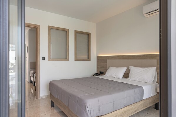 A modern bedroom with a wooden bed frame, a neutral color scheme, and a built-in air conditioning unit.