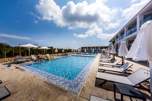 Una piscina con sillones de playa y sombrillas, rodeada por un edificio con ventanas amplias.