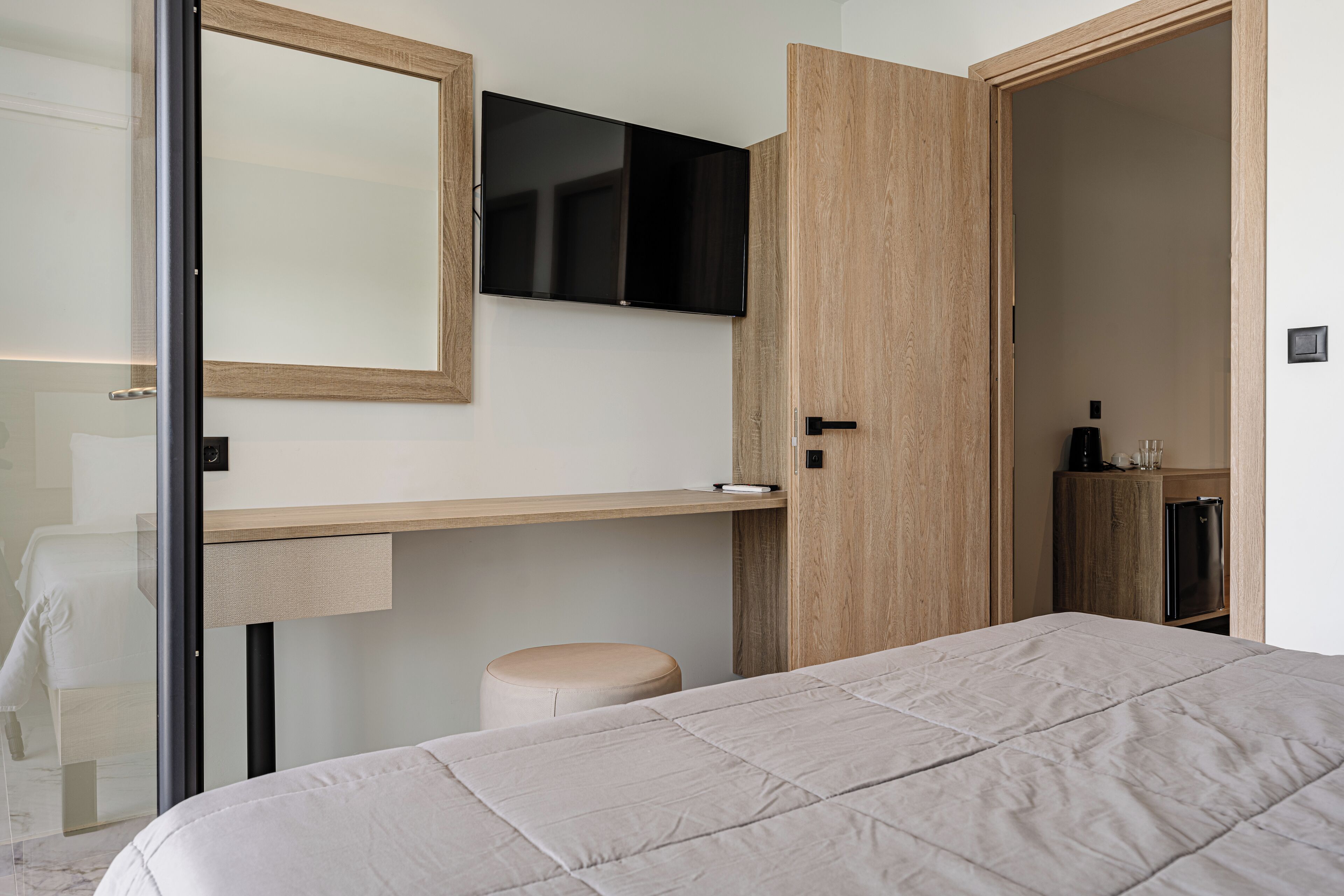 A modern bedroom with a bed, a wooden wardrobe, a flat-screen TV, and a small stool.