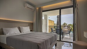 A modern hotel room with a large bed, a balcony with outdoor furniture, and a view of a building in the background. - Caretta Paradise Resort & Waterpark (Zakynthos)