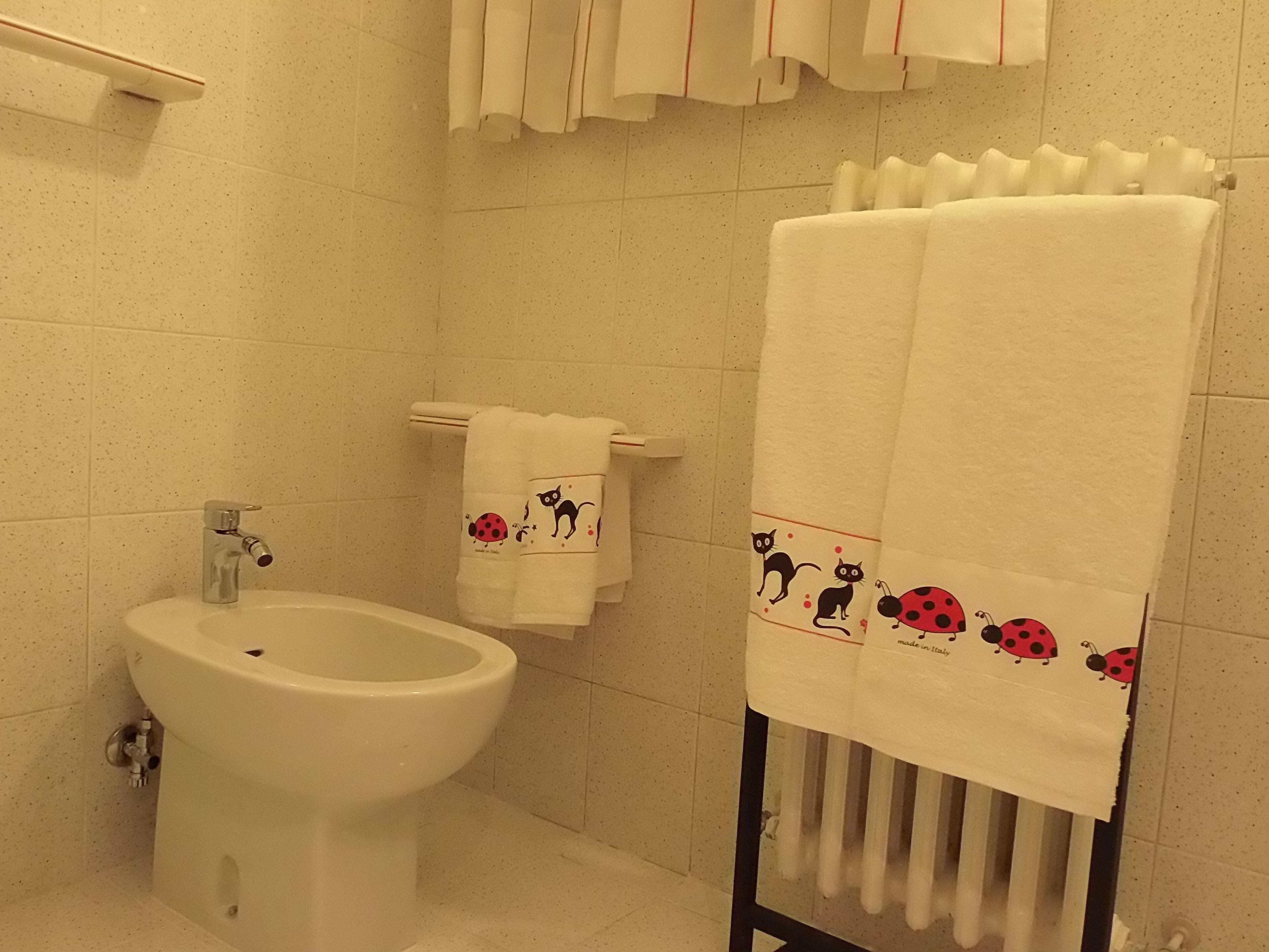 Un baño con bidé, un perchero con toalla que presenta diseños de mariquitas y un radiador.