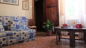 Un salon avec un canapé à motifs, une porte en bois, une plante en pot et une table sur laquelle sont posés des pots rouges.