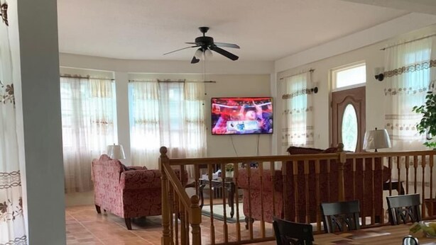 A dining area with a wooden table and chairs, a television mounted on the wall, and a staircase leading to another room.
