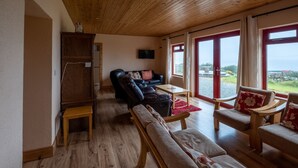 Un vaste espace de vie doté d’un plafond en bois, d’un canapé, d’un fauteuil, d’une petite table et d’un meuble.