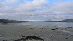 Une plage avec une mer calme, des collines lointaines et un ciel nuageux.