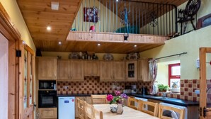 Un intérieur en bois comprenant une table à manger, des chaises et un coin cuisine avec des meubles de rangement en bois et un réfrigérateur.