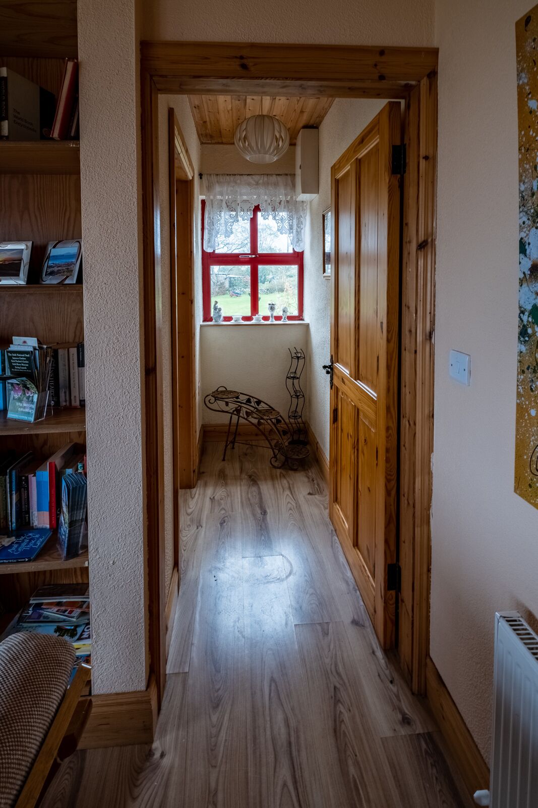 Un couloir étroit doté d’un plancher en bois et d’une fenêtre aux montants rouges.